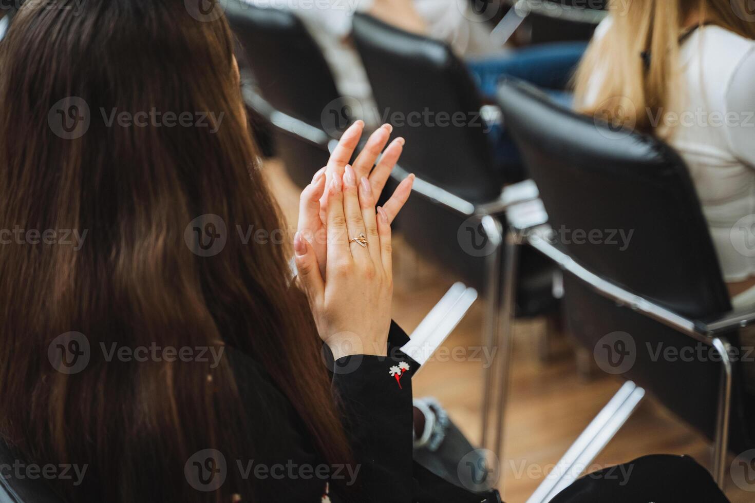 A woman sitting in a row of chairs clapping her hands in excitement photo