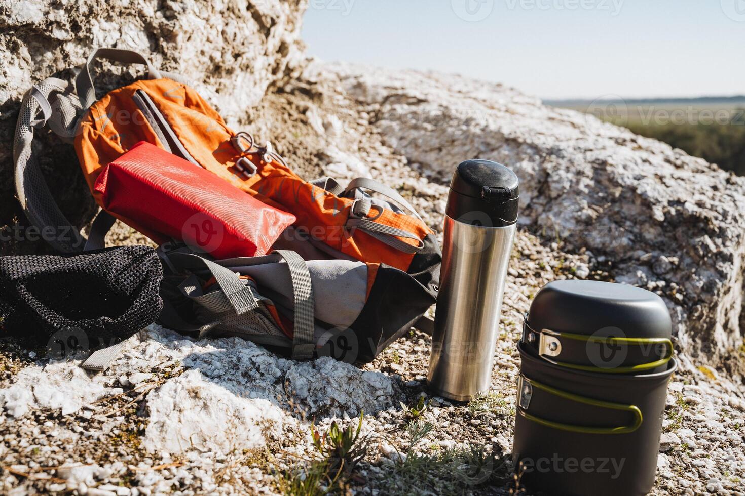 Outdoor Adventure Gear A sturdy Backpack, durable Thermos, and practical Food Container ready for exploration in a picturesque Rocky Landscape photo