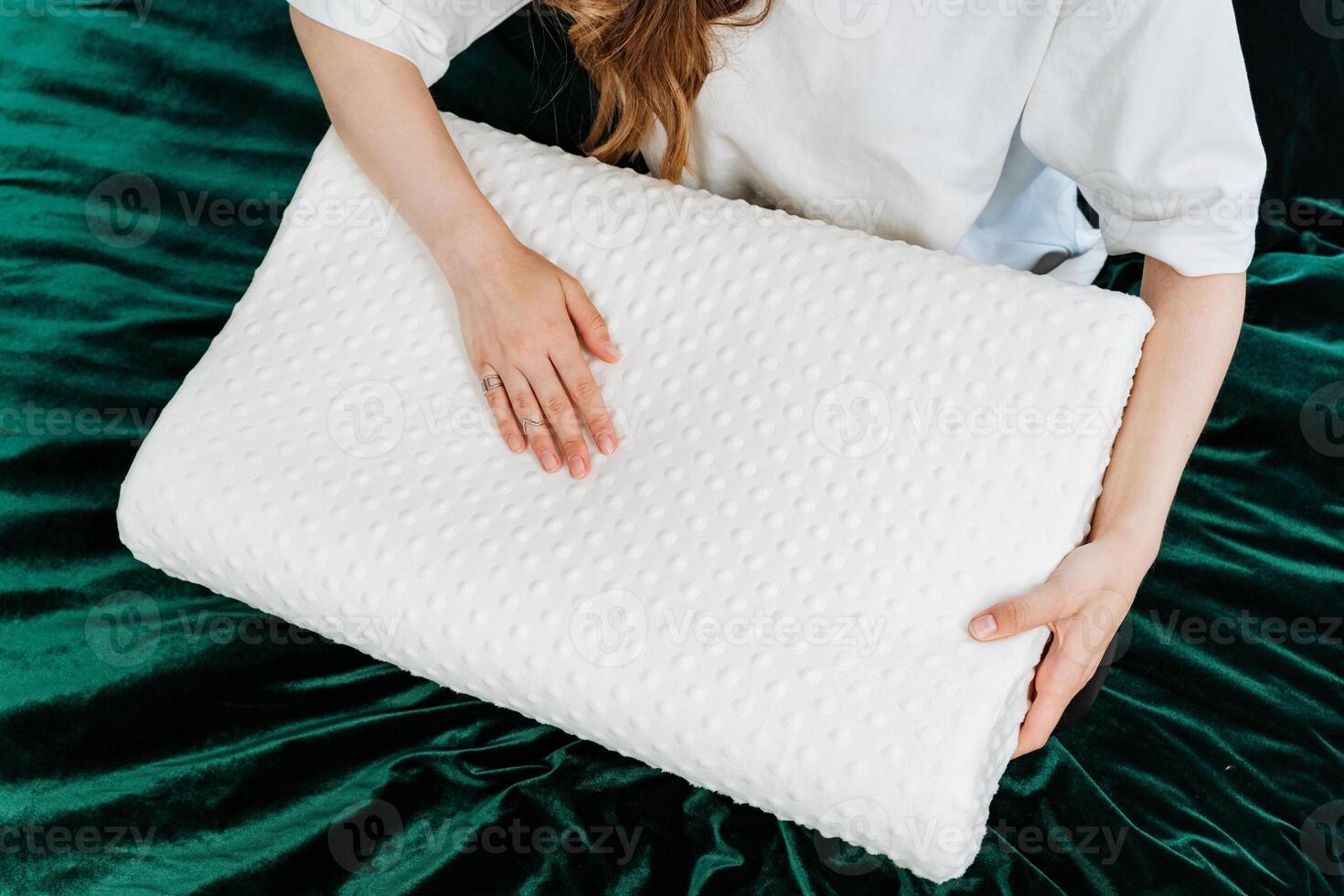 In a cozy bedroom, a woman enhances comfort and relaxation by holding an orthopedic memory foam pillow on a green velvet bedspread, creating a luxurious and modern setting photo