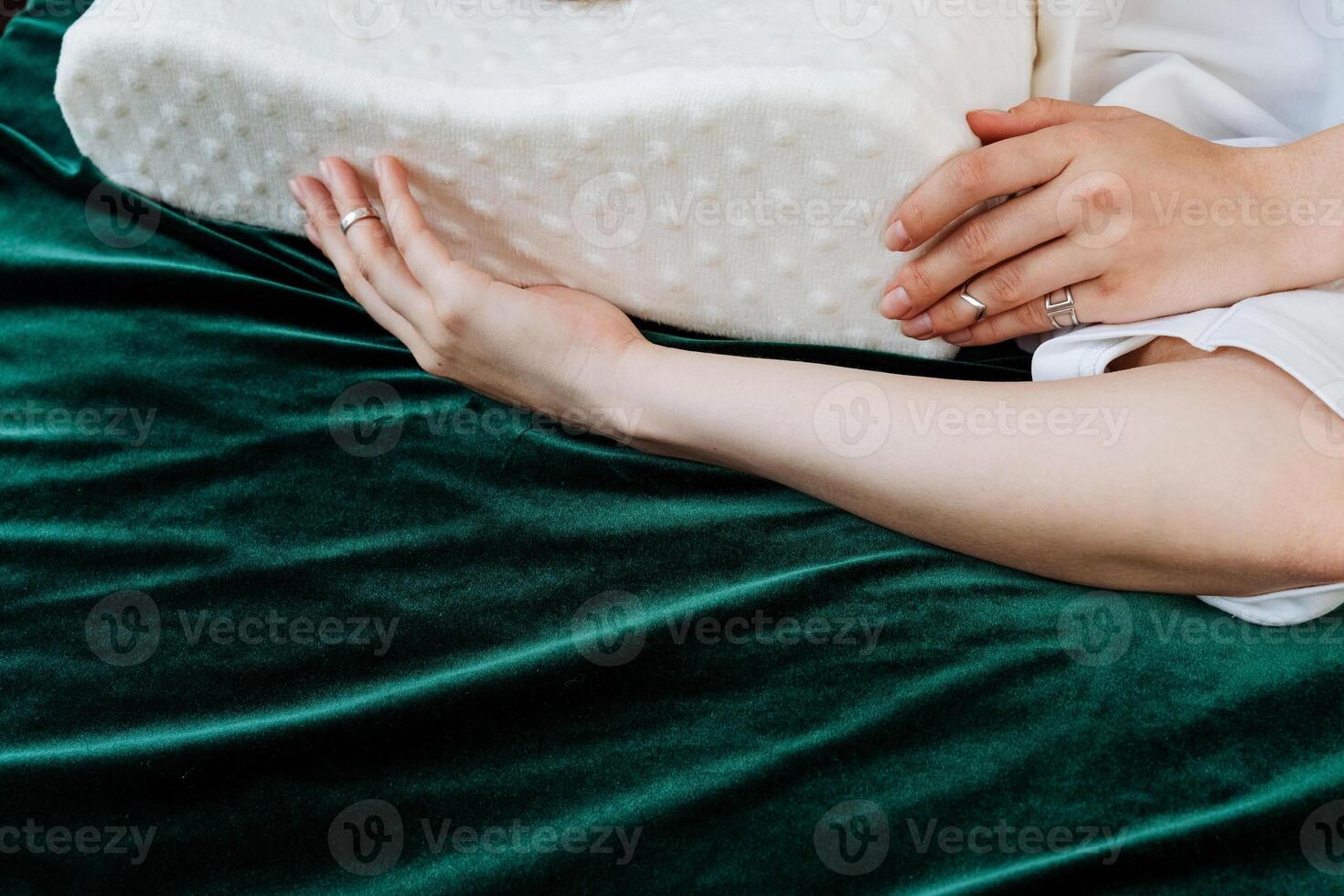A pair of hands delicately cradle a memory foam pillow on a lush green velvet bed, setting up a snug and restful ambiance for ultimate relaxation and rejuvenation photo