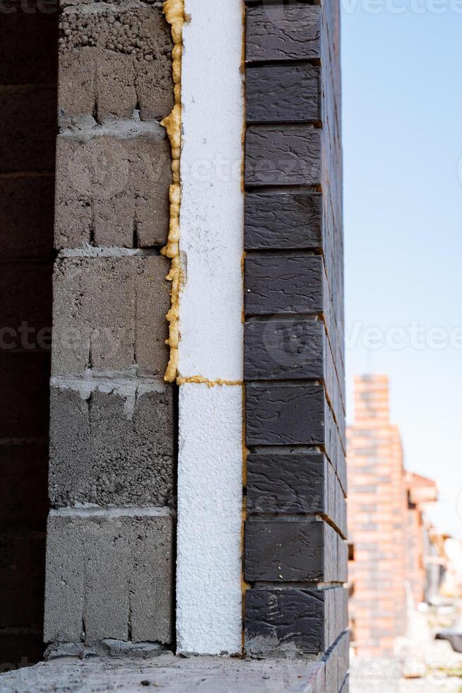 A brick wall with a piece of styrofoam stands against the sky, showcasing a mix of building materials and textures on the facade, including brickwork and composite materials photo