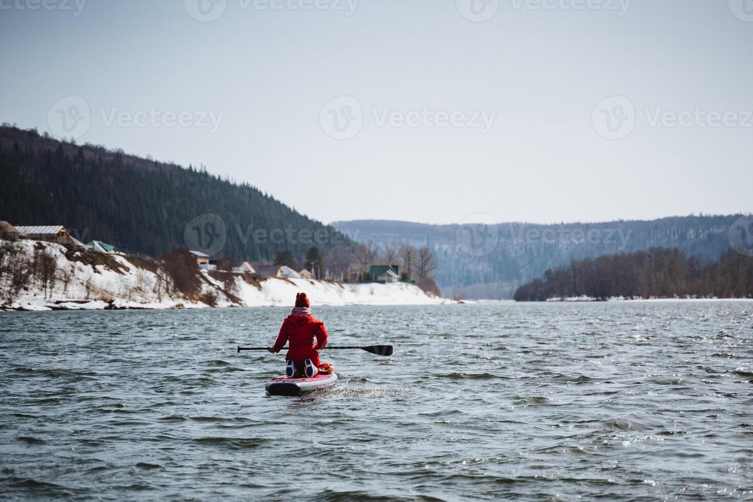 Rear view of a SUP board floating on the river against the background of mountains, tourist rafting alone on a SUP board, board with a paddle, spring hike, extreme on the water. photo