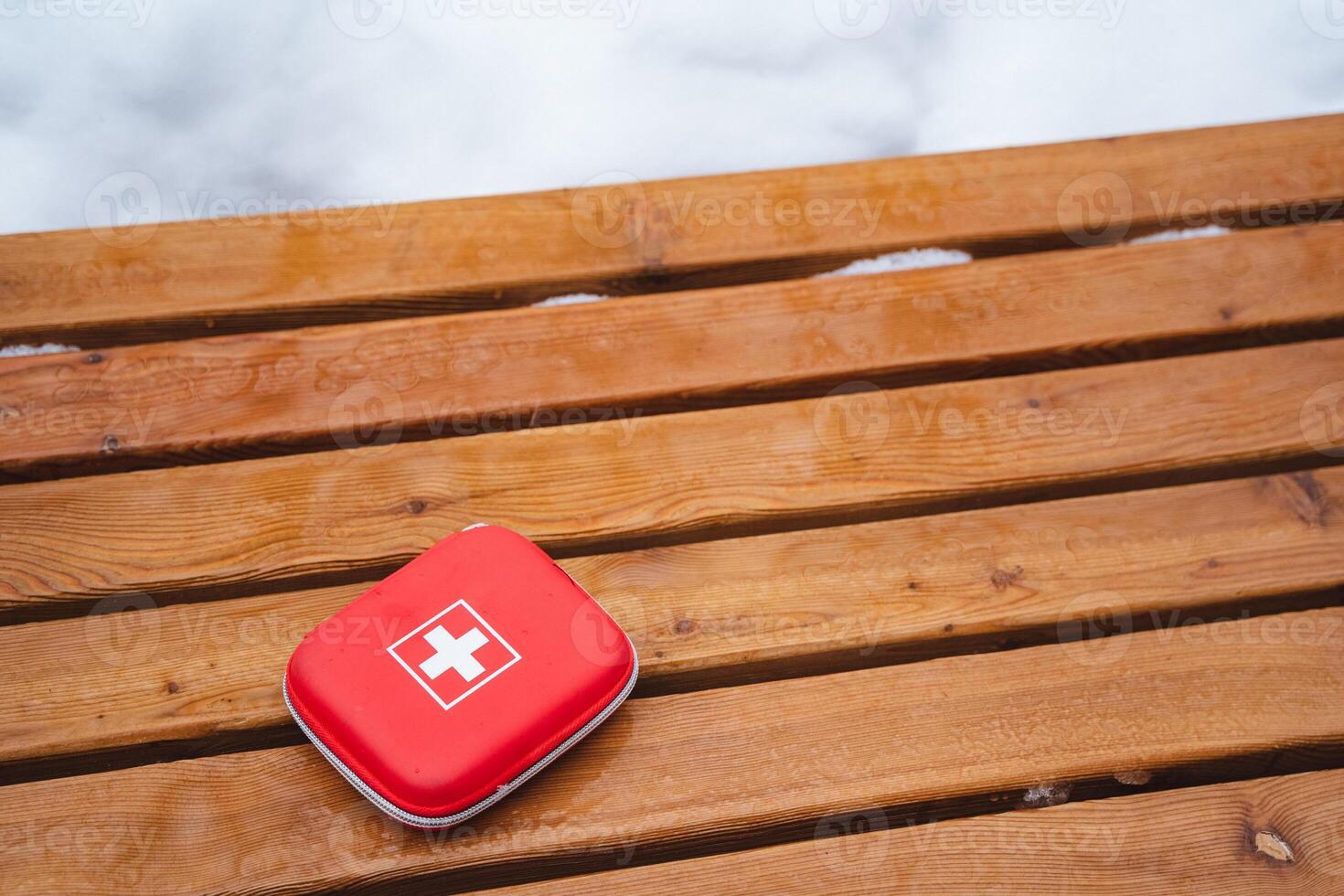A bright red first aid kit is resting on a beautifully crafted wooden table, which features a rich wood stain and a fine varnish finish, showcasing the natural beauty of the hardwood plank photo