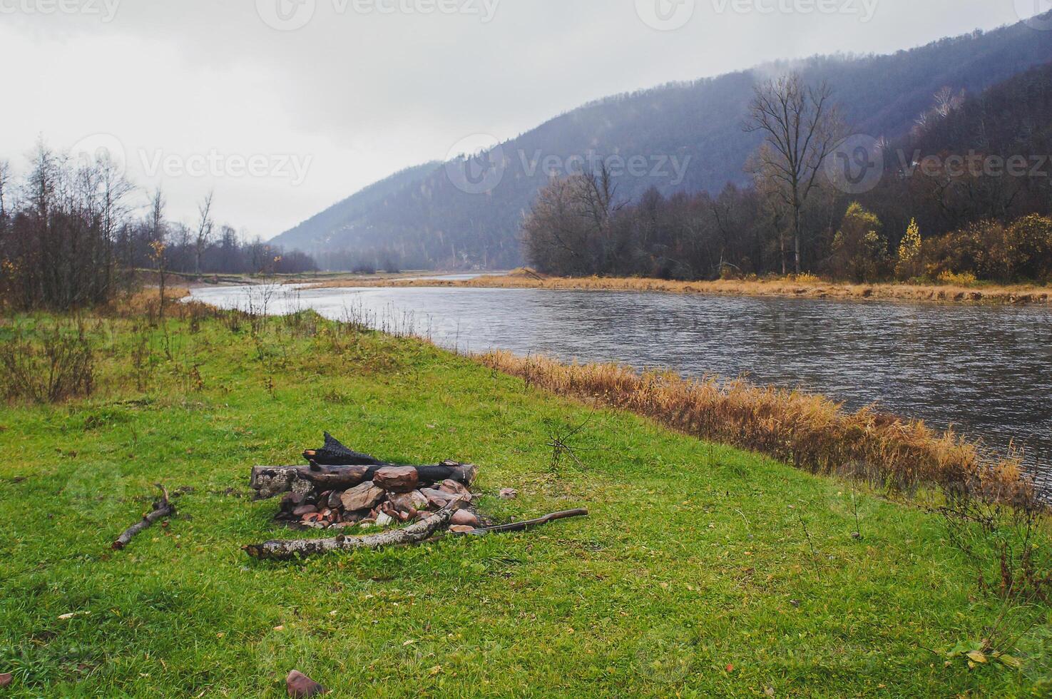 A campfire under the sky, next to a river bank surrounded by grass and trees photo