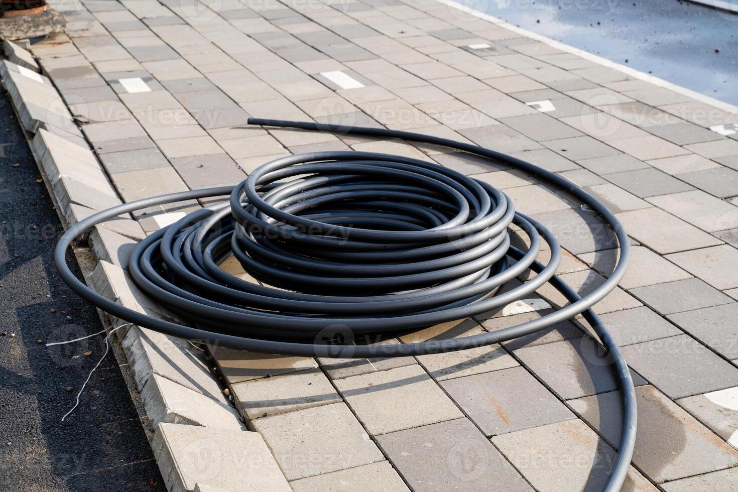 A coiled black hose is strategically positioned on a paved surface at a bustling construction site for various purposes photo