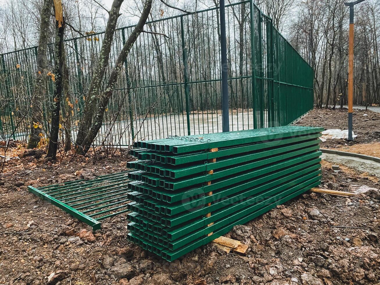 A tall stack of green metal scaffolding is currently sitting inconspicuously in the dirt right next to a rustic fence that lines the area. It makes for an interesting outdoor sight photo