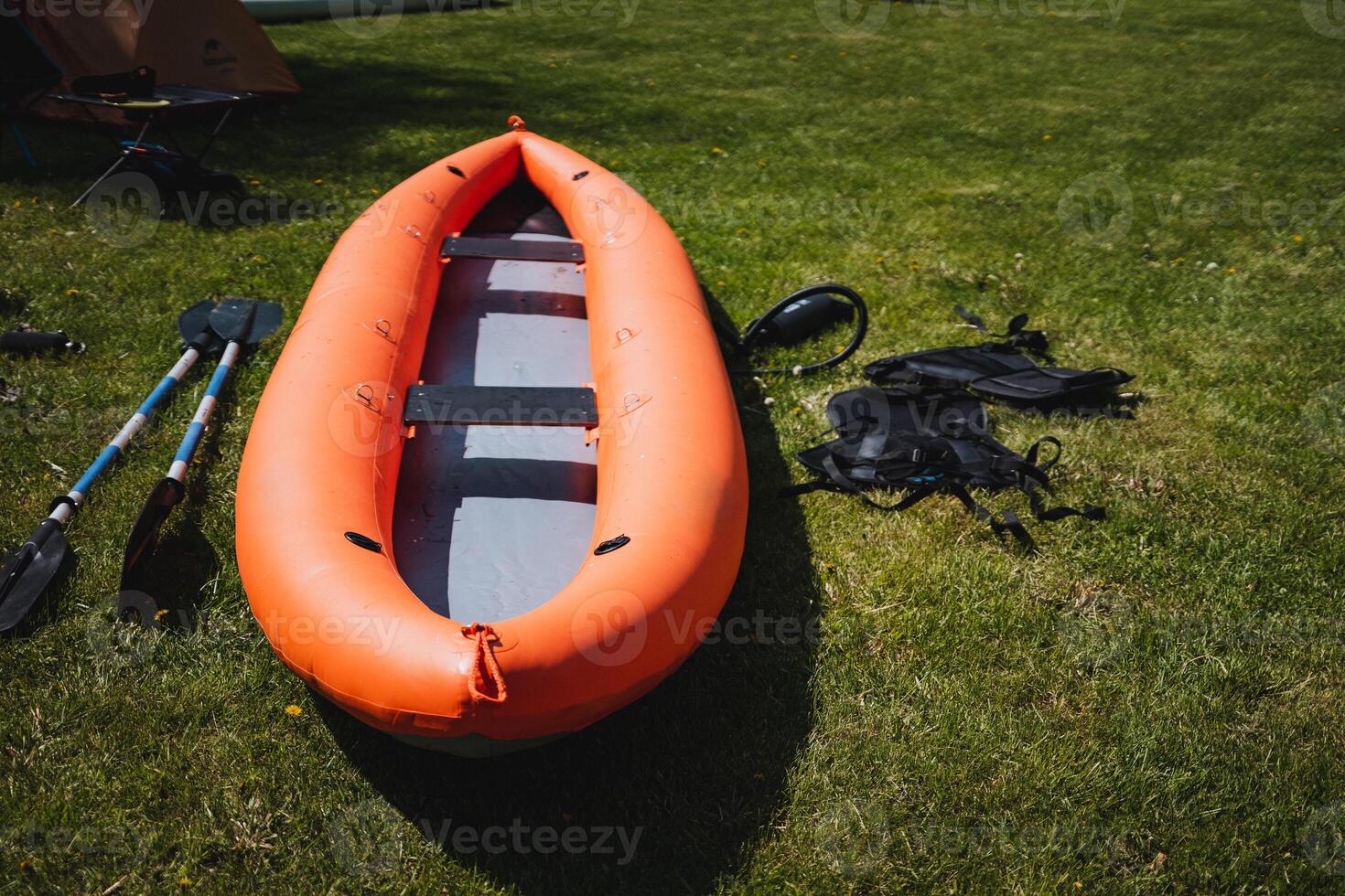 An orange inflatable kayak with paddles and gear is resting on green grass in a sunny park, suggesting outdoor recreation and water sports like kayaking and boating photo