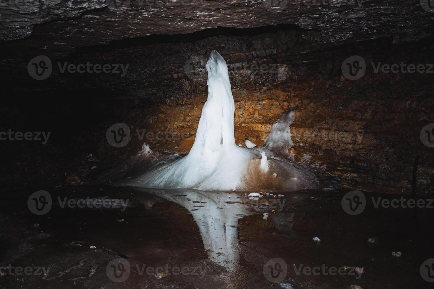Stalactite ice formations can be discovered in a dark cave, where their stunning beauty is reflected on the surface of the water beneath them photo