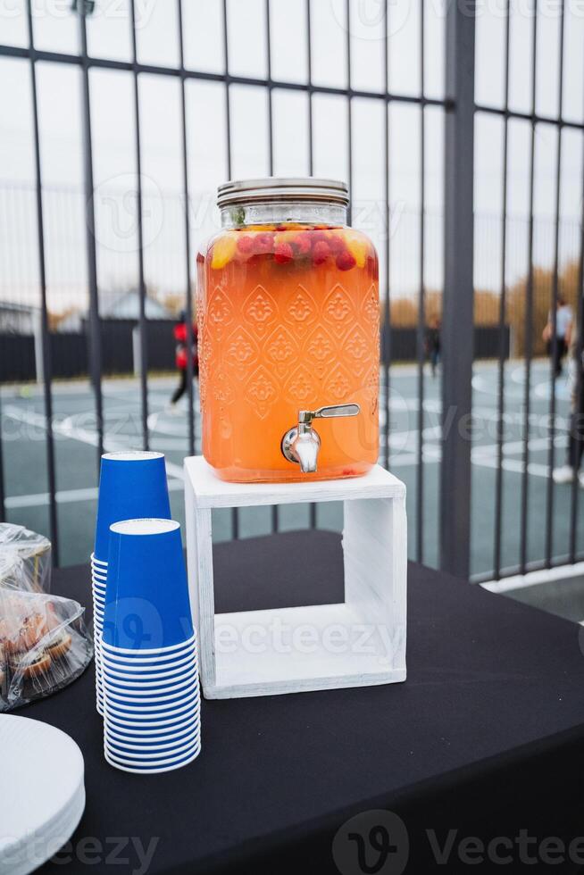 A spacious table in the room features a stylish drink dispenser and neatly arranged electric blue cups, ready to serve refreshing beverages for the guests of the gathering photo