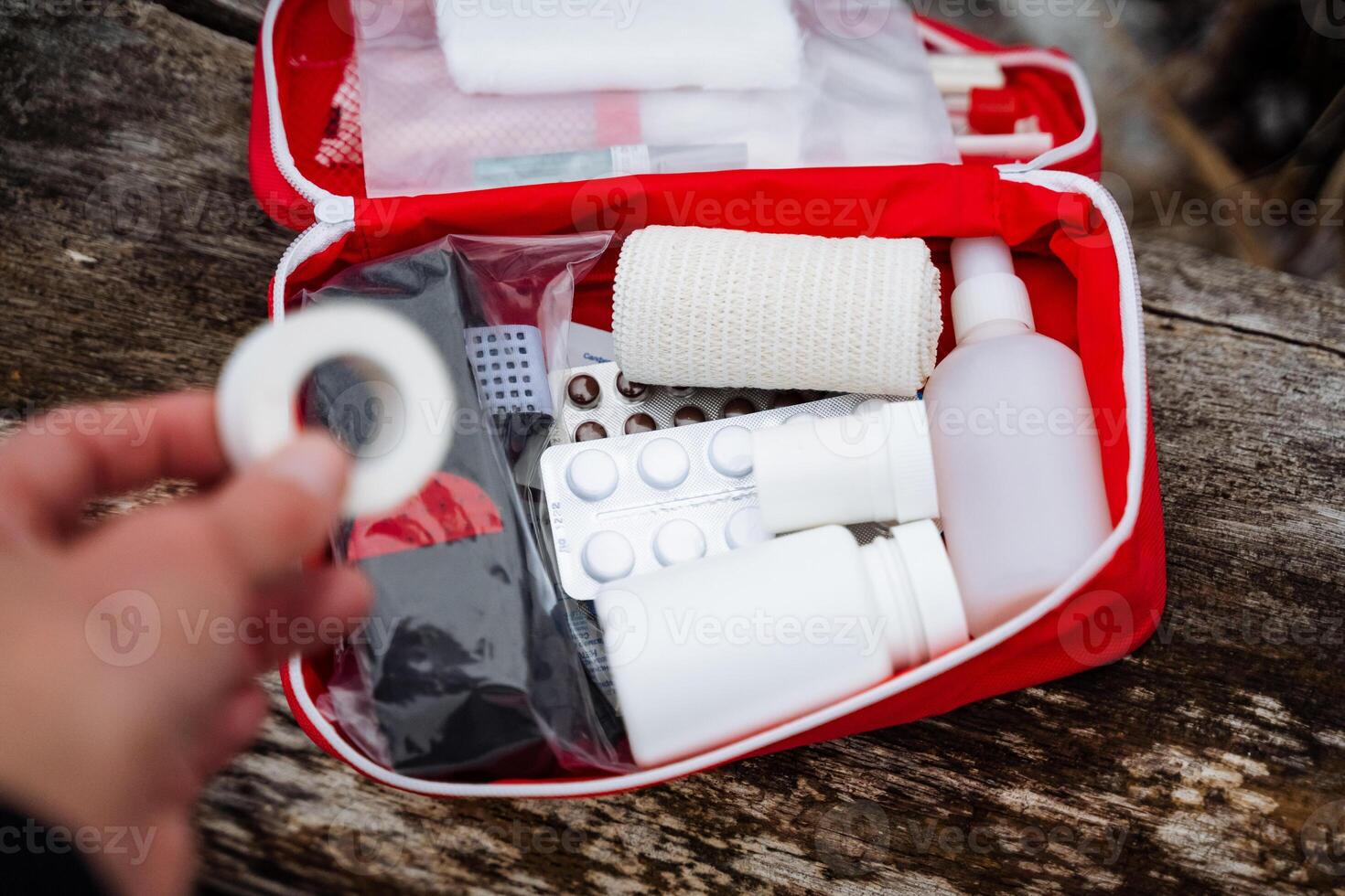 A person is currently holding a bandage while positioned right in front of an open first aid kit, suggesting readiness for any potential medical emergencies that may arise photo