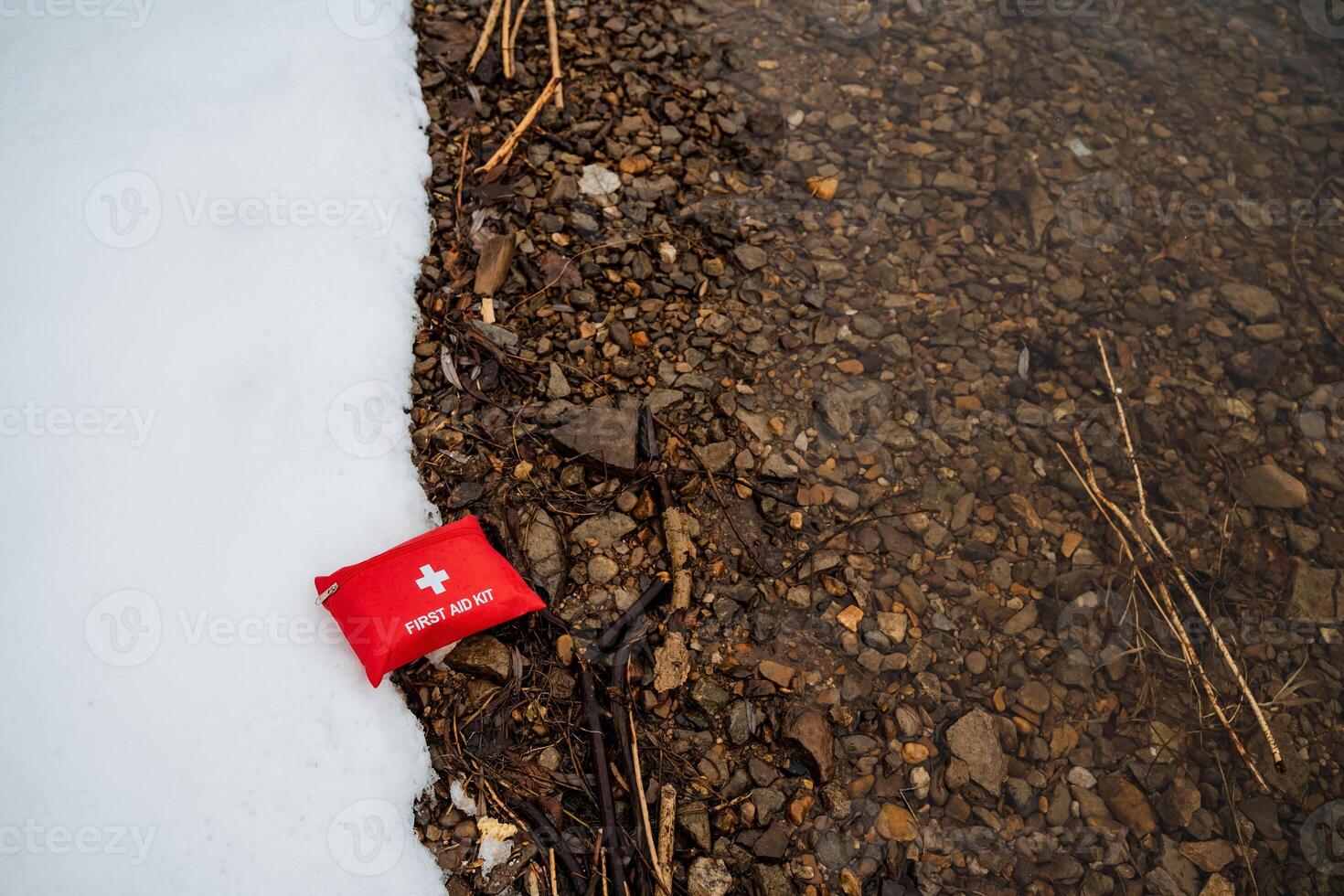 A bright red first aid kit has been inexplicably placed on the ground, creating a striking and vivid contrast against the surrounding elements of both nature and the urban scenery around it photo