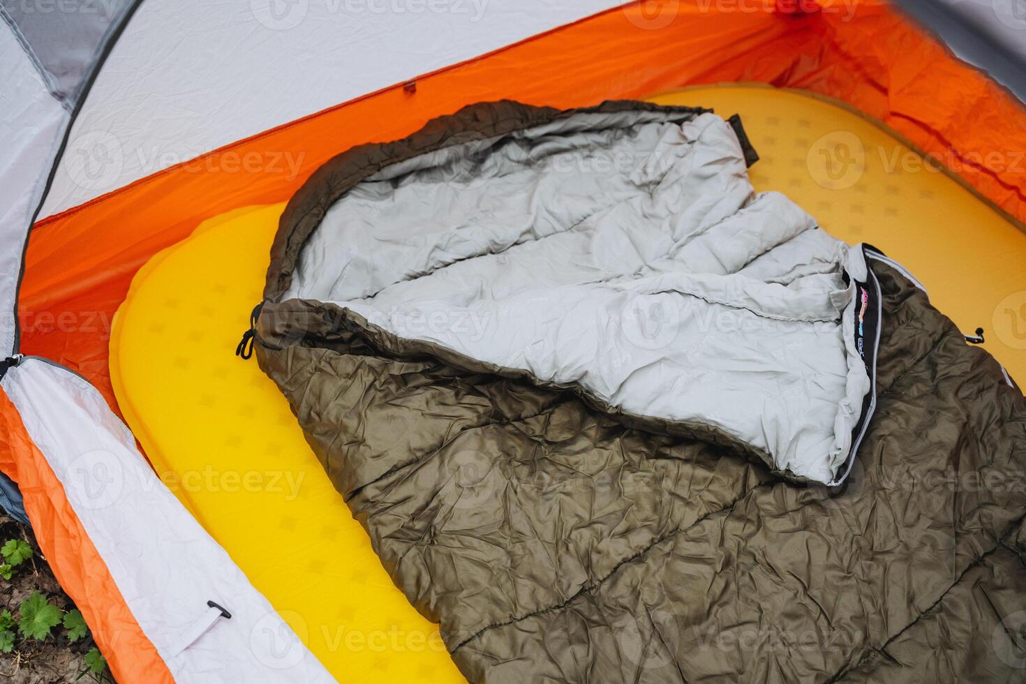 A sleeping bag rests on a yellow mattress inside a tent photo