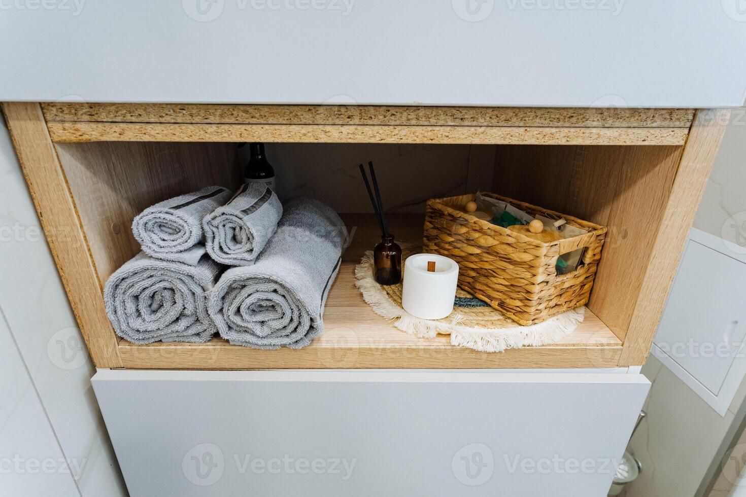 A wellorganized bathroom cabinet is expertly packed with neatly folded towels of various sizes, rolls of soft toilet paper, and an attractive basket that serves multiple storage purposes photo