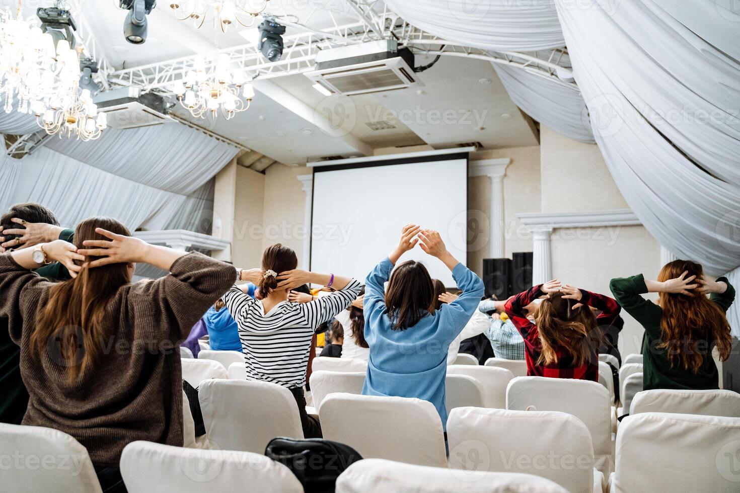 Crowd in chairs watching projector screen during event photo