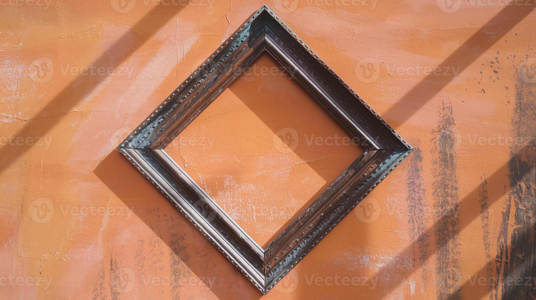 Empty Diagonal Wooden Frame Hanging on Vibrant Orange Grunge Wall with Shadows and Sunlight photo