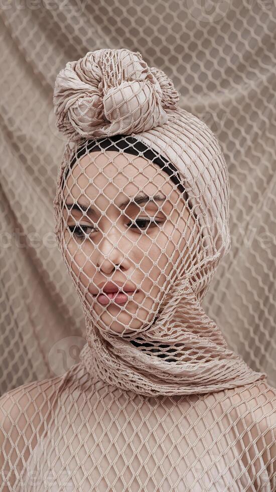 Artistic Portrait of Woman with Neutral Tones Wrapped in Textured Mesh Fabric and Minimal Background photo