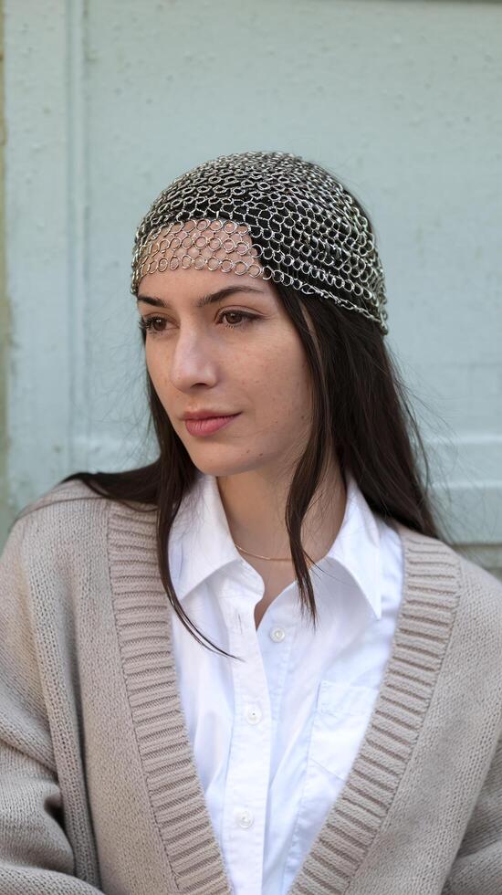 Woman Wearing Chainmail Headpiece with Beige Sweater and White Shirt Front of Light Teal Wall photo