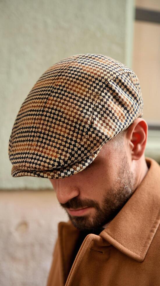 Closeup of Man Wearing Retro Houndstooth Pattern Flat Cap and Brown Wool Coat Outdoors Near Wall photo