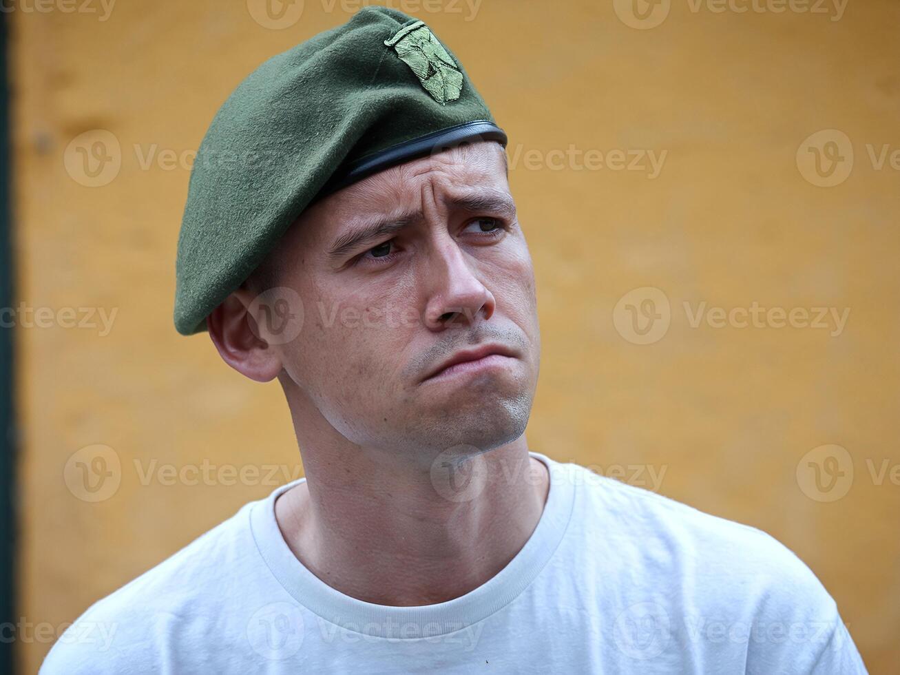 Serious Man Wearing Green Military Beret with Yellow Wall Background Expressing Determination photo