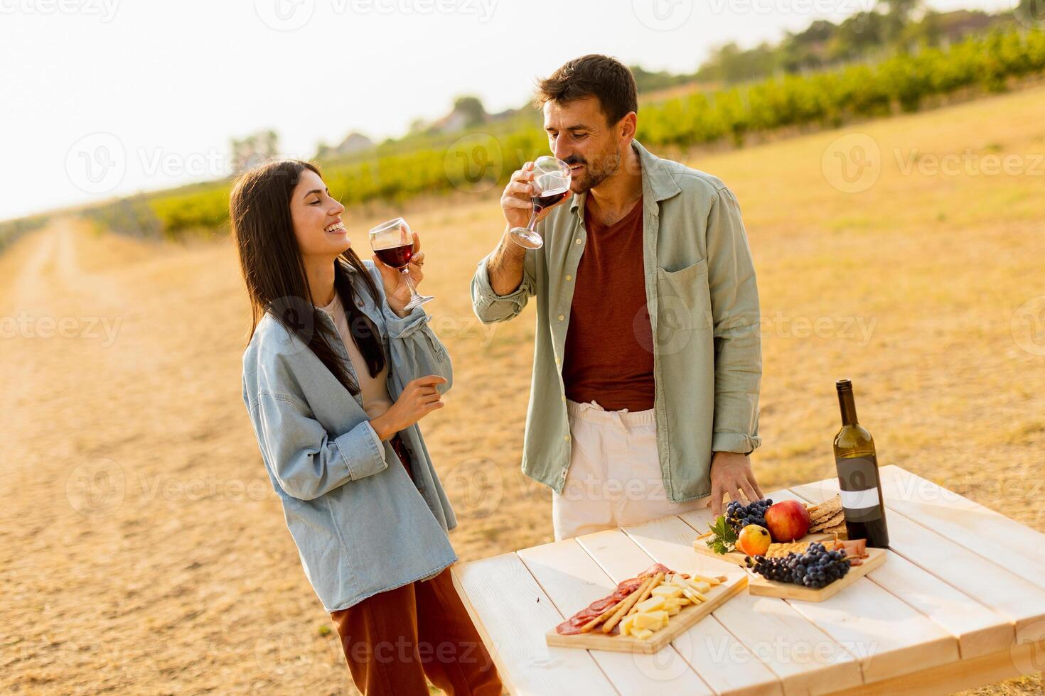 Romantic picnic in a sunlit vineyard featuring a couple enjoying wine and a gourmet platter among vines during golden hour photo