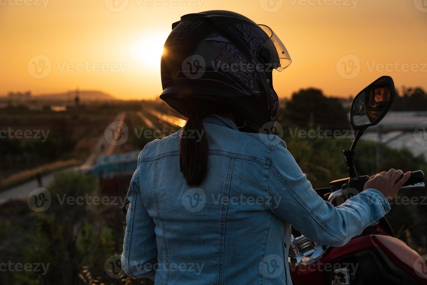 Woman with helmet and on a motorcycle observes the landscape illuminated by the rays of the sun. photo