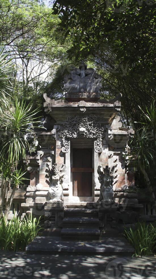 Traditional Balinese temple gate with intricate stone carvings and guardian statues surrounded by lush greenery and natural light in a serene outdoor setting in Bali photo