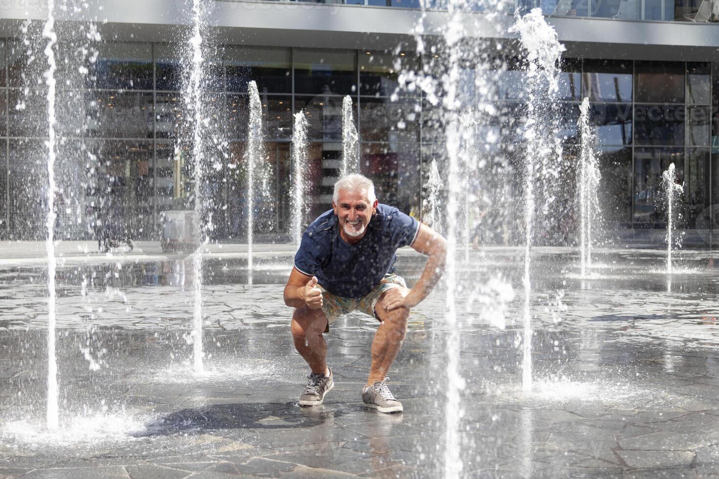 middle-aged man having fun like a child among the splashes of water of a modern fountain in an Italian capital photo
