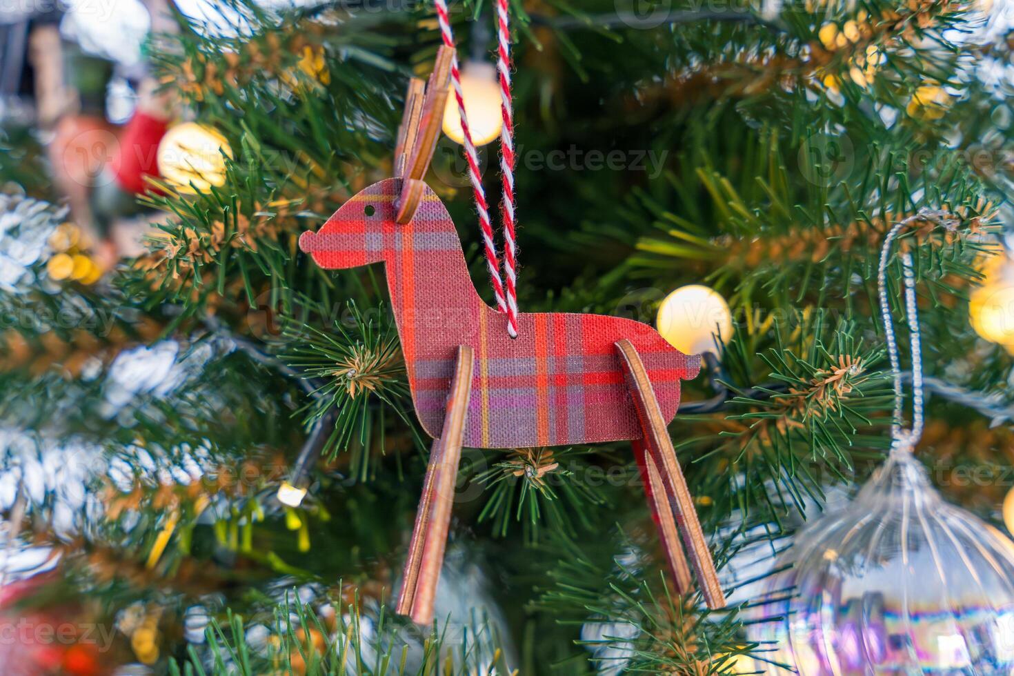 Red wooden reindeer ornament with plaid pattern on an artificial Christmas tree with warm lights photo