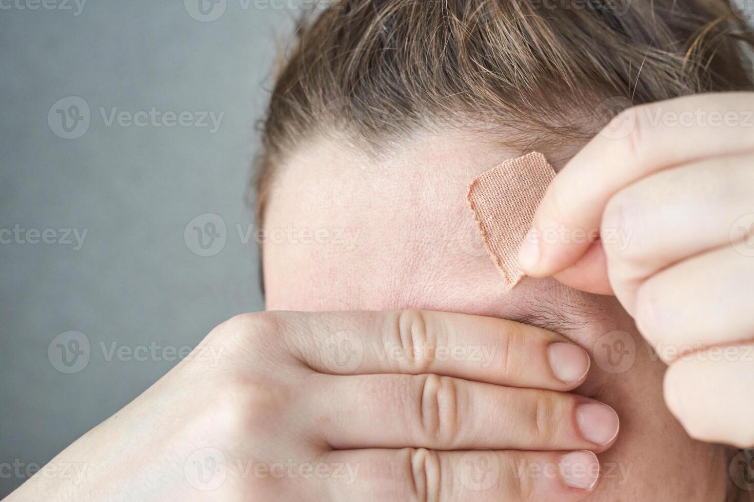 Female adult with bandage on forehead covering eyes with hand healthcare, healing, injury concept. photo