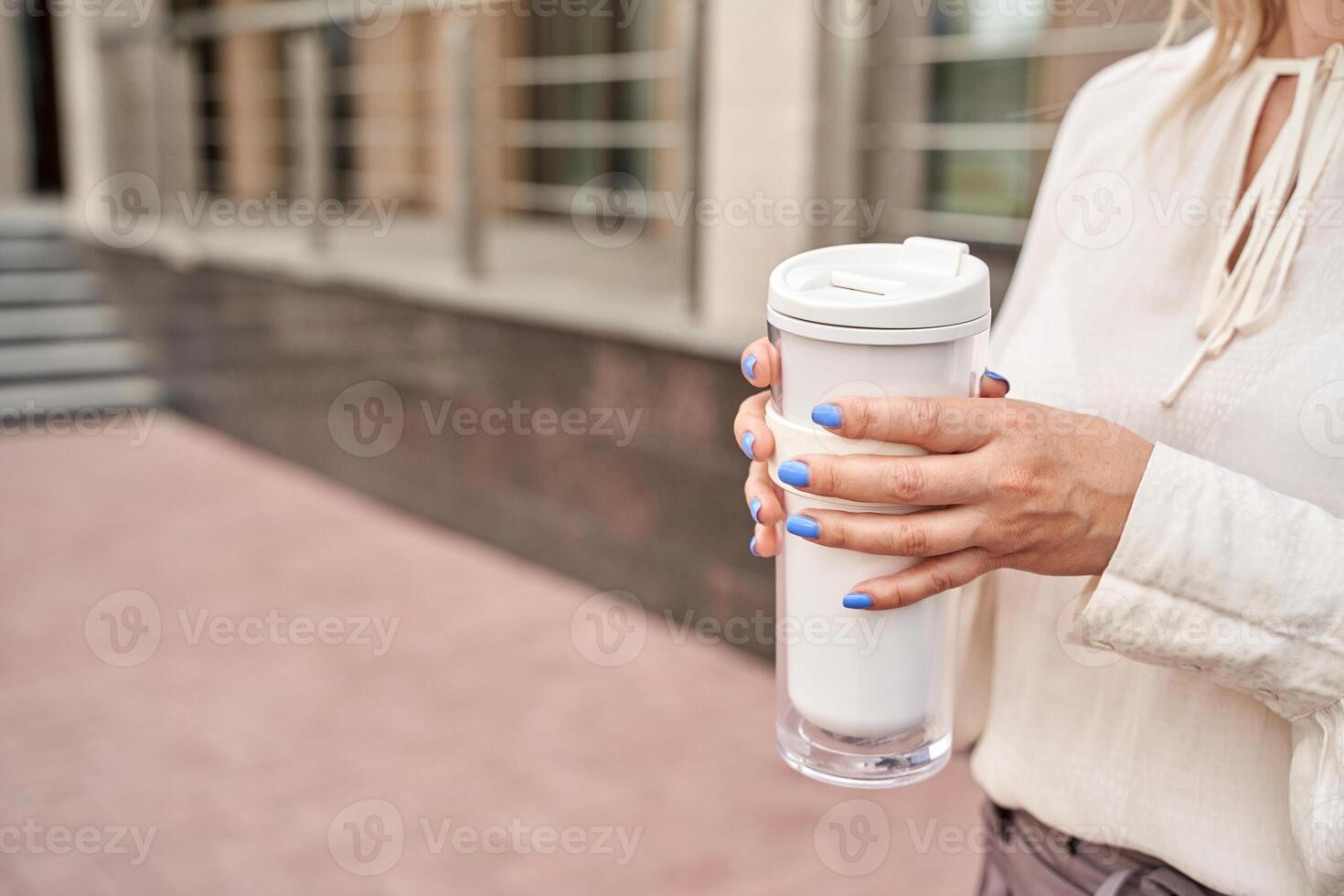 Caucasian female with light blue nails holding coffee tumbler outdoors urban setting. photo