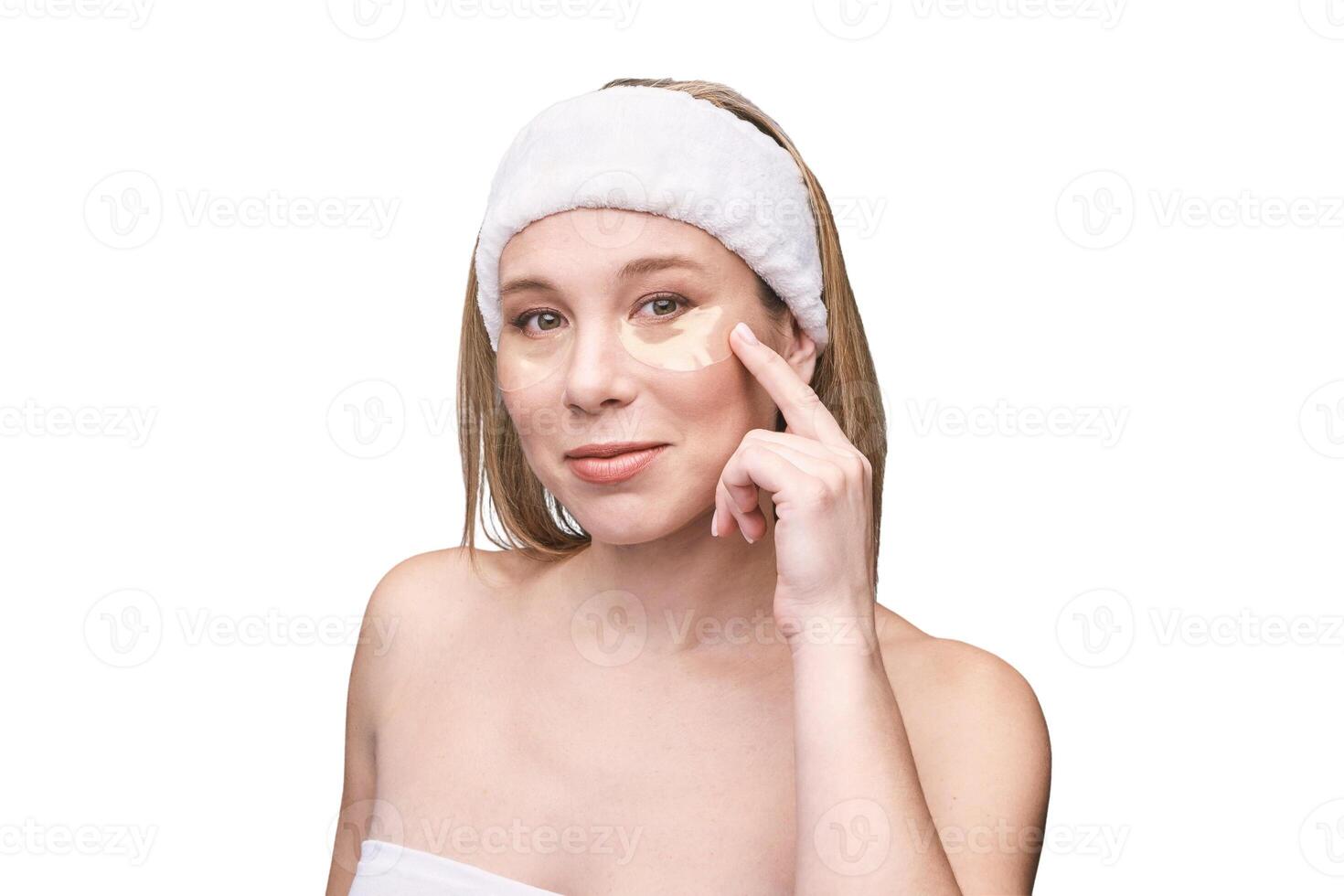 Caucasian female adult applying under eye mask for skincare routine with headband and bare shoulders. photo