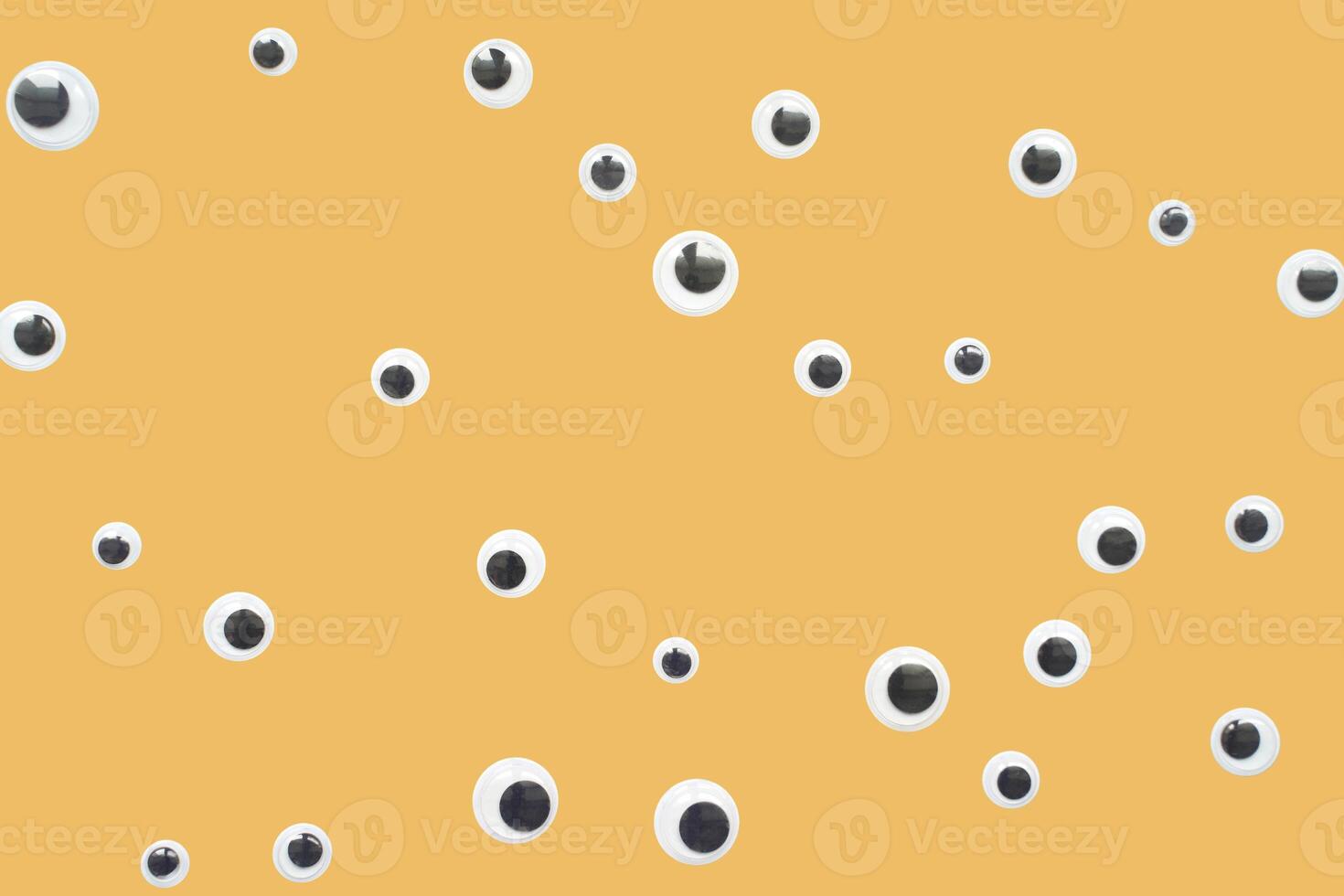 Scattered googly eyes on yellow background with playful and creative design elements. photo