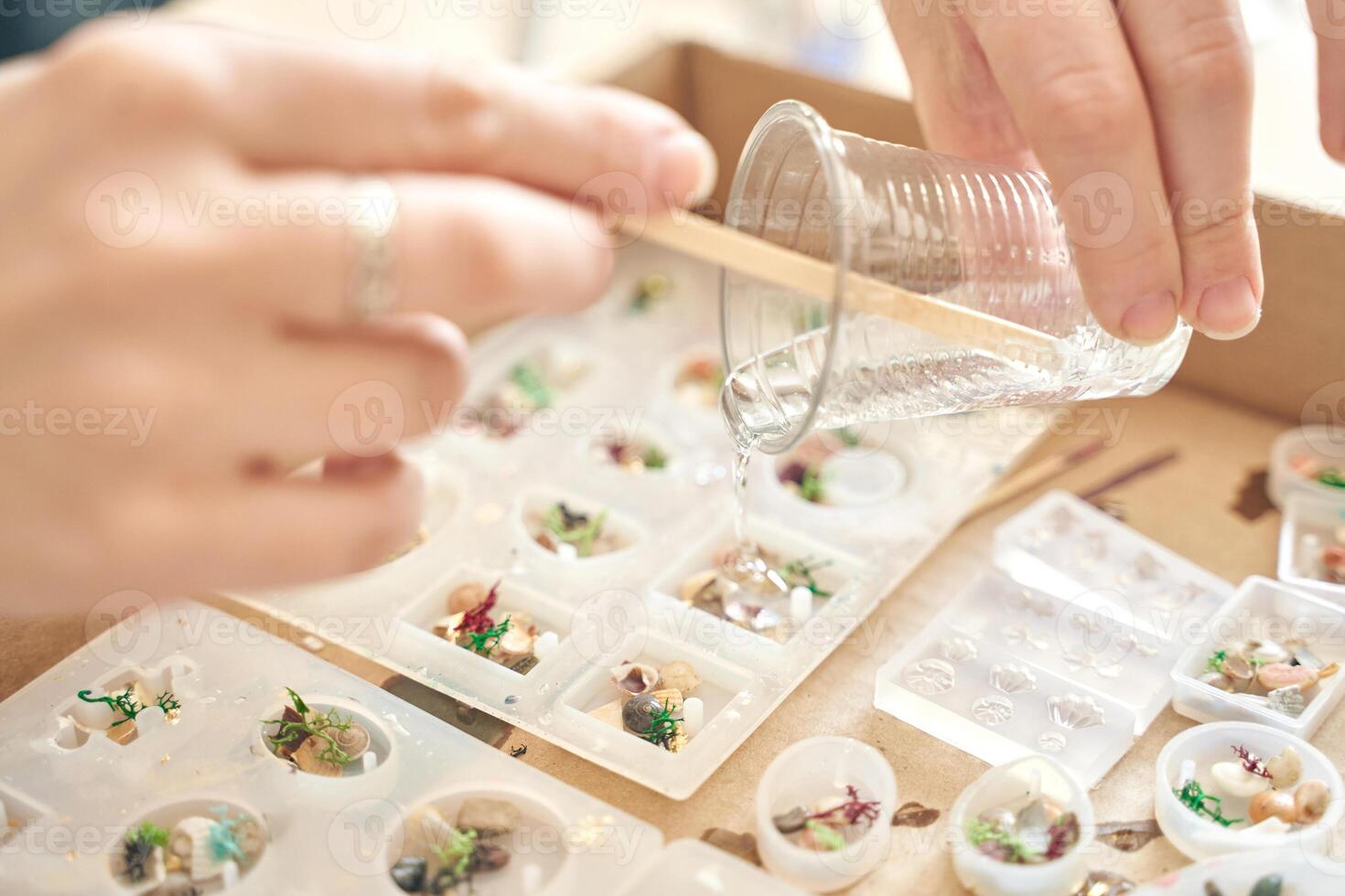 Hands pouring resin into molds for artistic jewelry making at craft workshop. photo