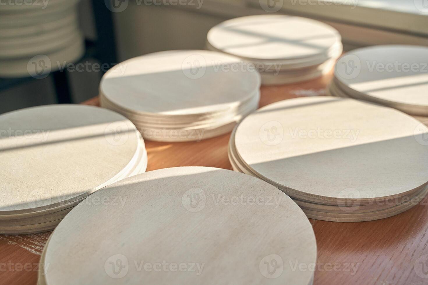 Sunlit wooden circles stacked on table in workshop with natural light shadows. photo