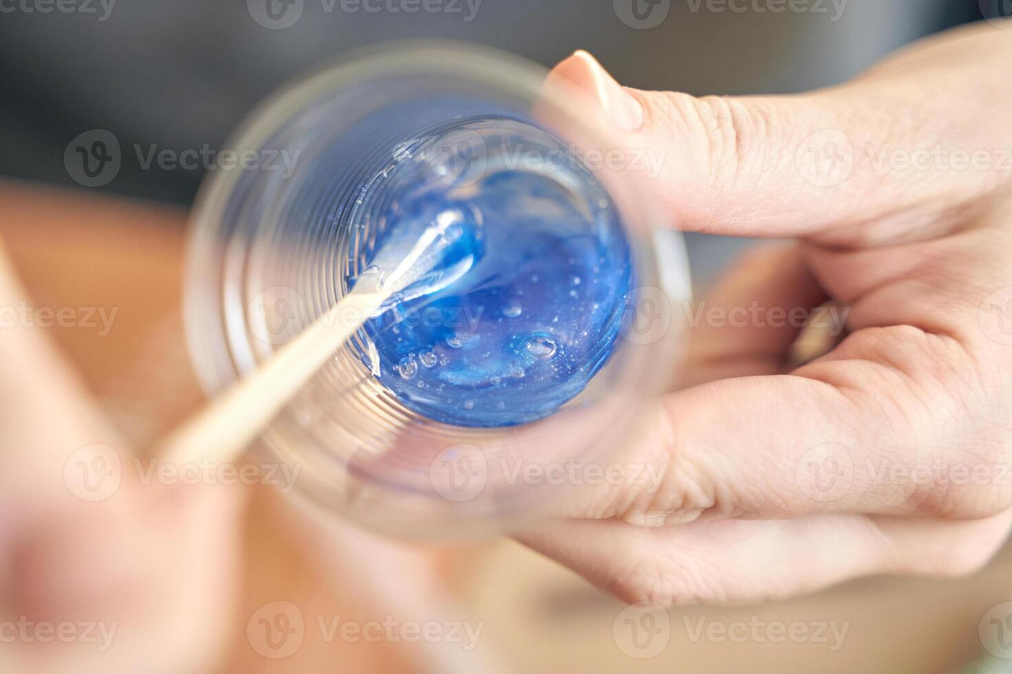 Close up of hands mixing blue epoxy resin in clear plastic cup with wooden stick. photo