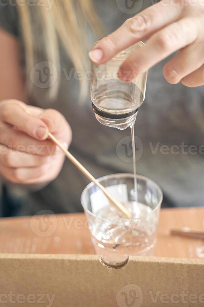 Young caucasian female mixing resin in a cup using a wooden stick for craft projects. photo