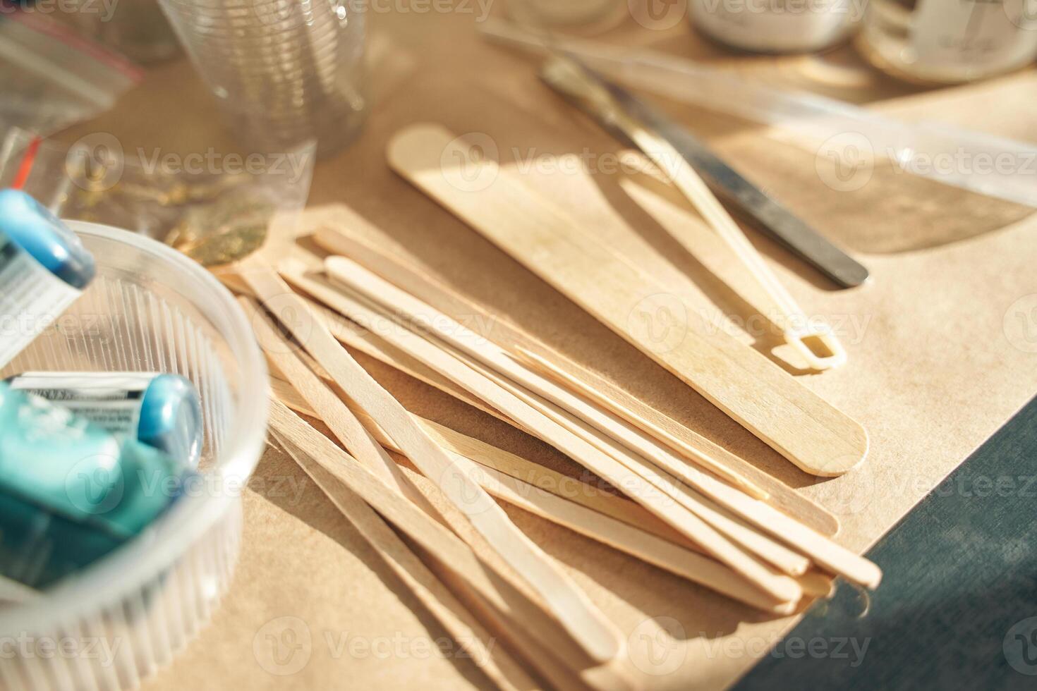 Wooden craft sticks and tools arranged on a workshop table with blue glue tubes in sunlight. photo