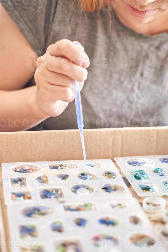 Young caucasian female crafting diy resin jewelry using silicone molds and pipette. photo