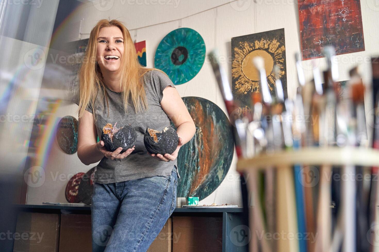Caucasian female artist showcasing art in studio with paintings and brushes displayed in creative environment. photo