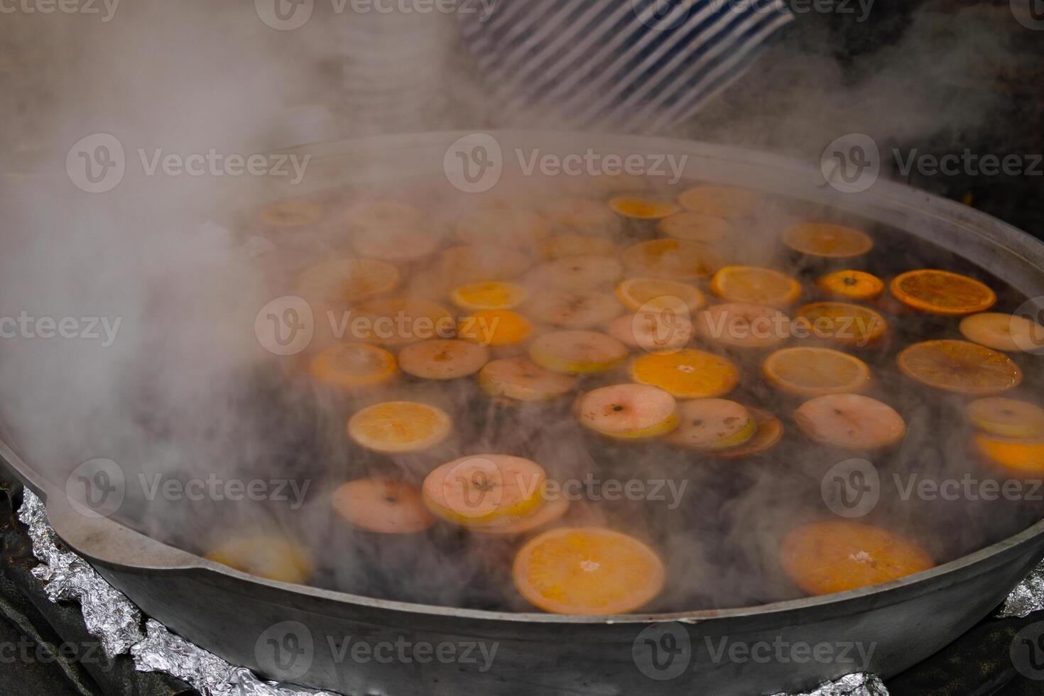 mulled wine with apples and oranges is brewed in a street food cauldron photo