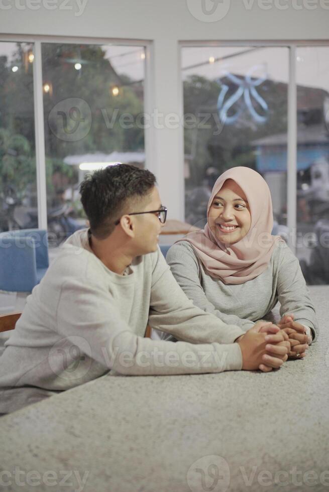 beautiful asian muslim woman giving a glass of juice to her husband at home photo
