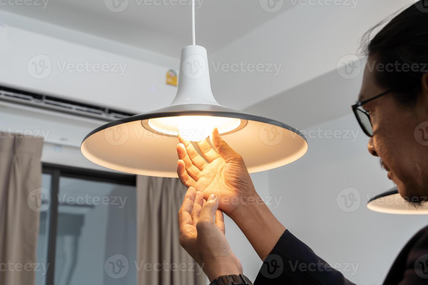 Happy man changing a light bulb at home. High angle shot of a young man in a checkered shirt standing on a step ladder and placing. photo
