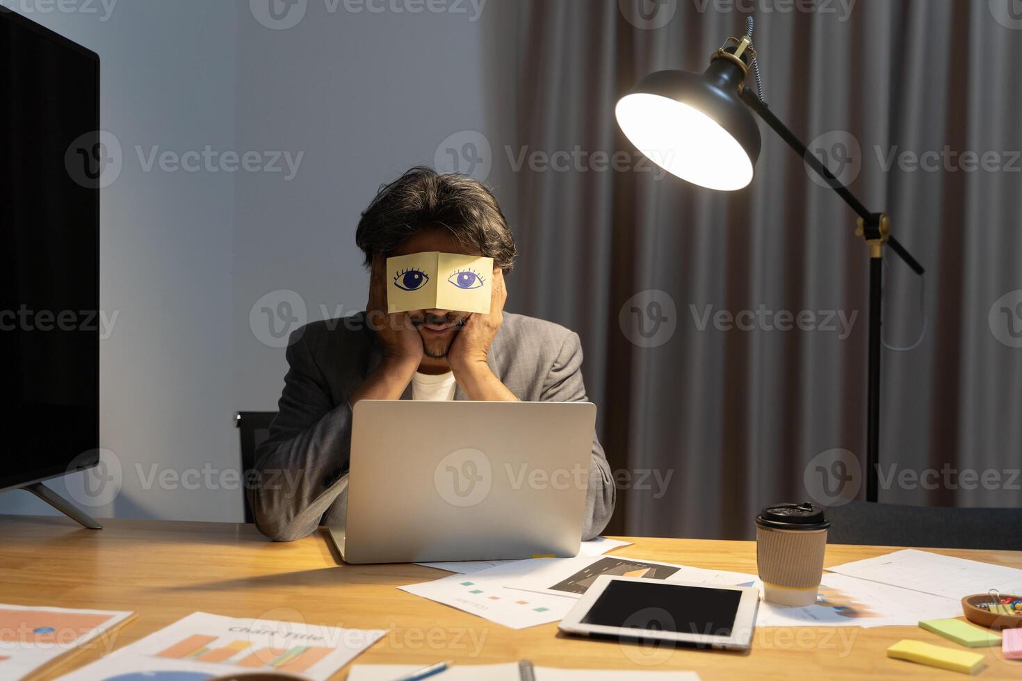 Exhausted young Caucasian man worker have sticker pads on eyes sleeping near computer in office. Tired millennial male employee fall asleep doze off at workplace. photo