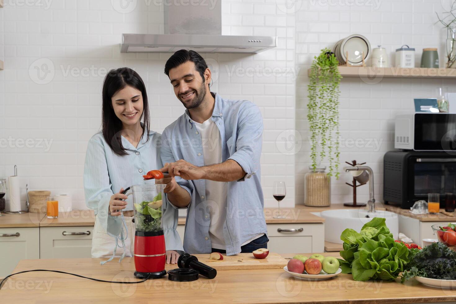Young couple mixing fruit in a food processor, making a smoothie. Husband and wife having fun with smoothie in the kitchen and looking at each other. photo