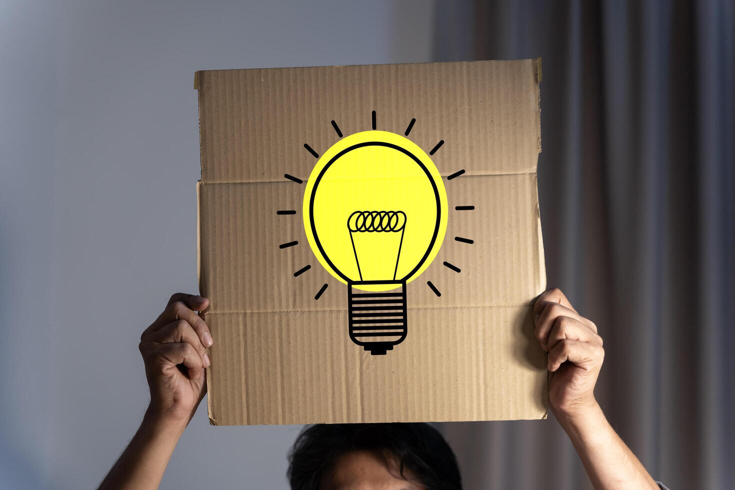 Conceptual image of businessman gesturing with a cardboard box on his head with light bulb. Businessman holding a sign with light bulb, concept of the idea. photo