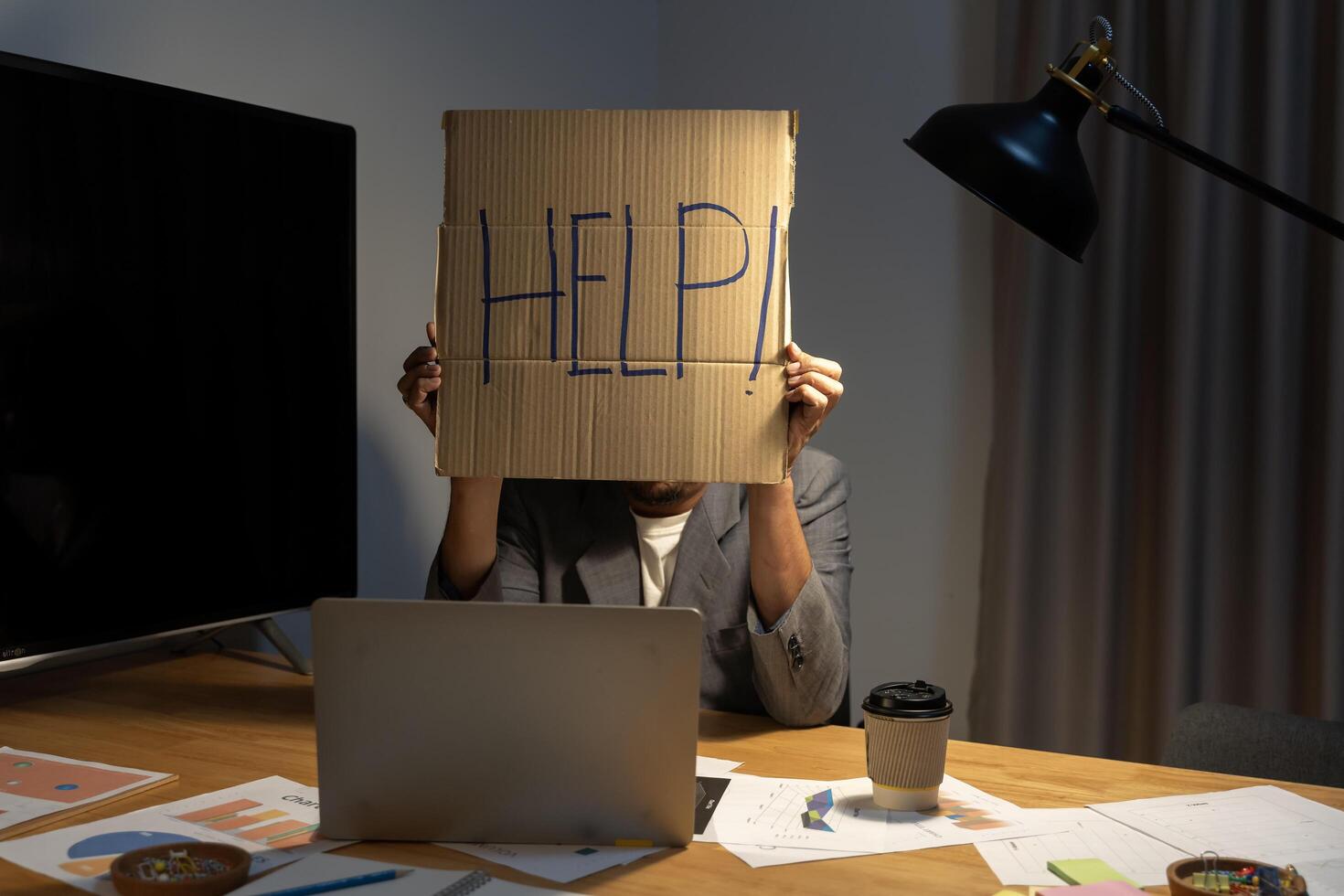 Young Businessman Holding Cardboard With Help Text At Workplace. Young Asian businessman working with stress at laptop computer desk. photo