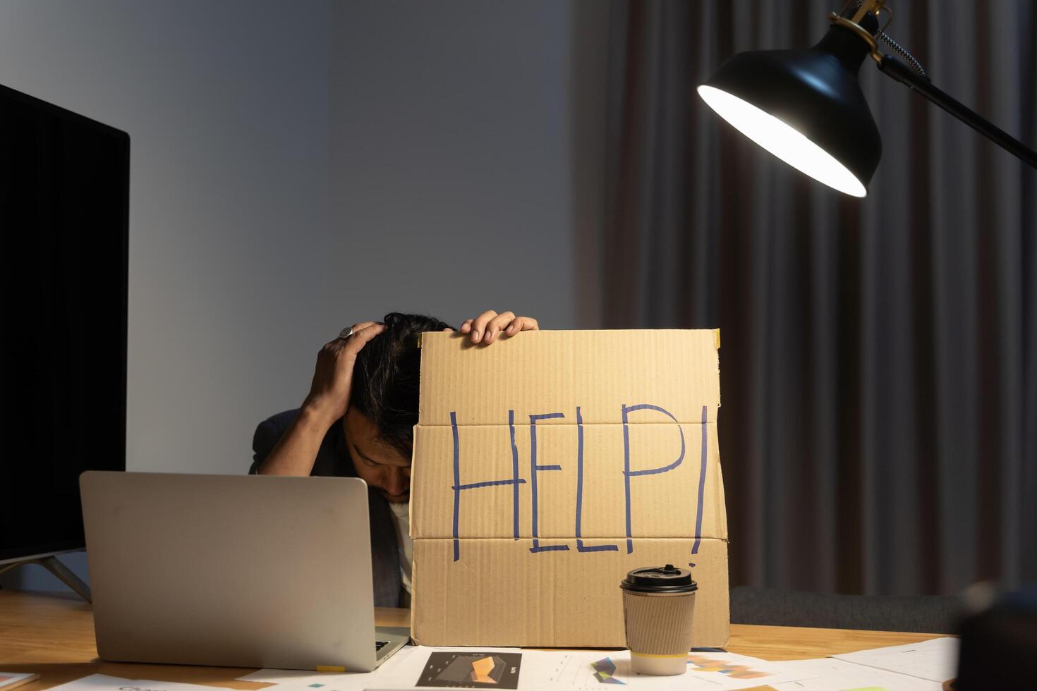 Frustrated and overworked businessman holding his head with a laptop computer and asking for help in office at night. photo