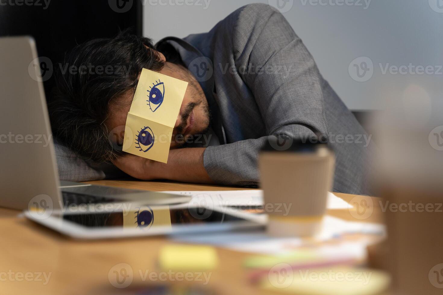 Cheerful adult man resting in office with sticky notes on the eyes. Sleeping man having stickers with eyes painted on face. photo