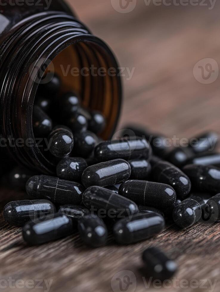 Black capsules spilled from an open bottle on a wooden surface photo