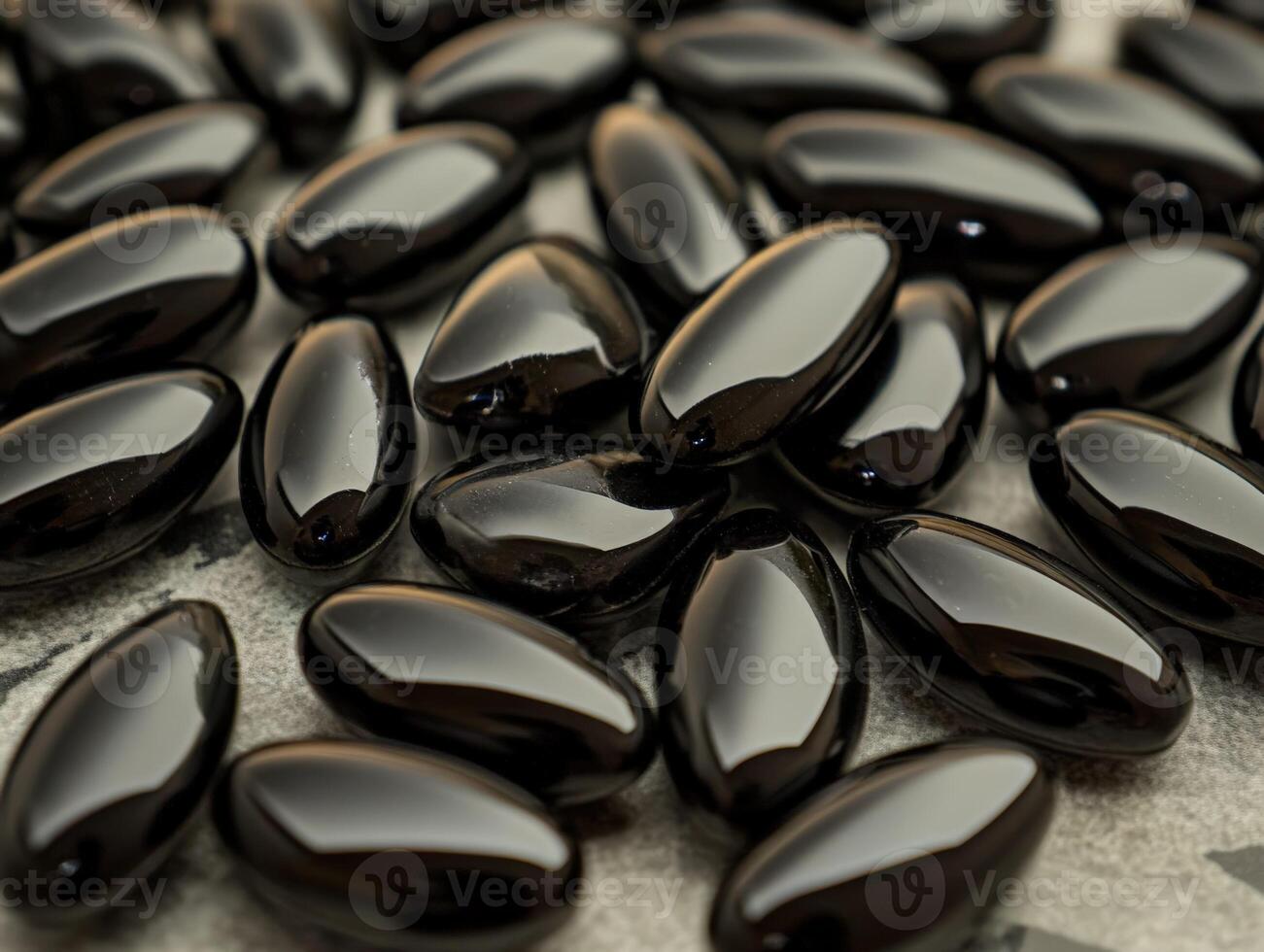 Black glossy capsules scattered on a textured surface in natural light photo